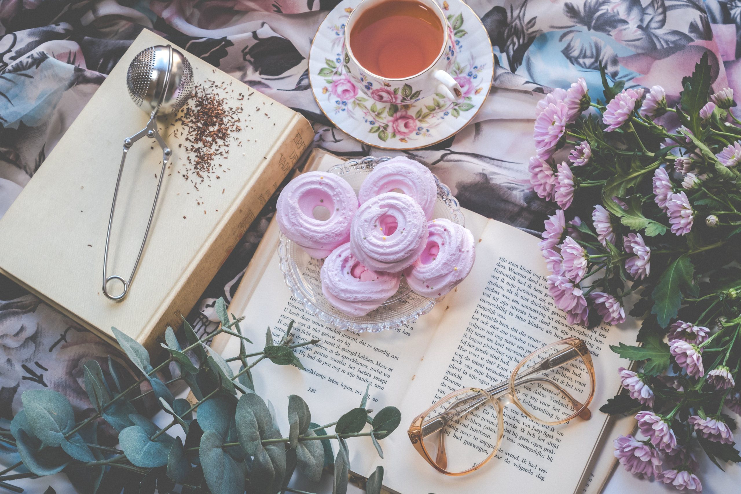 tea and a pink sweet treat on a book that is on a bed of flowers