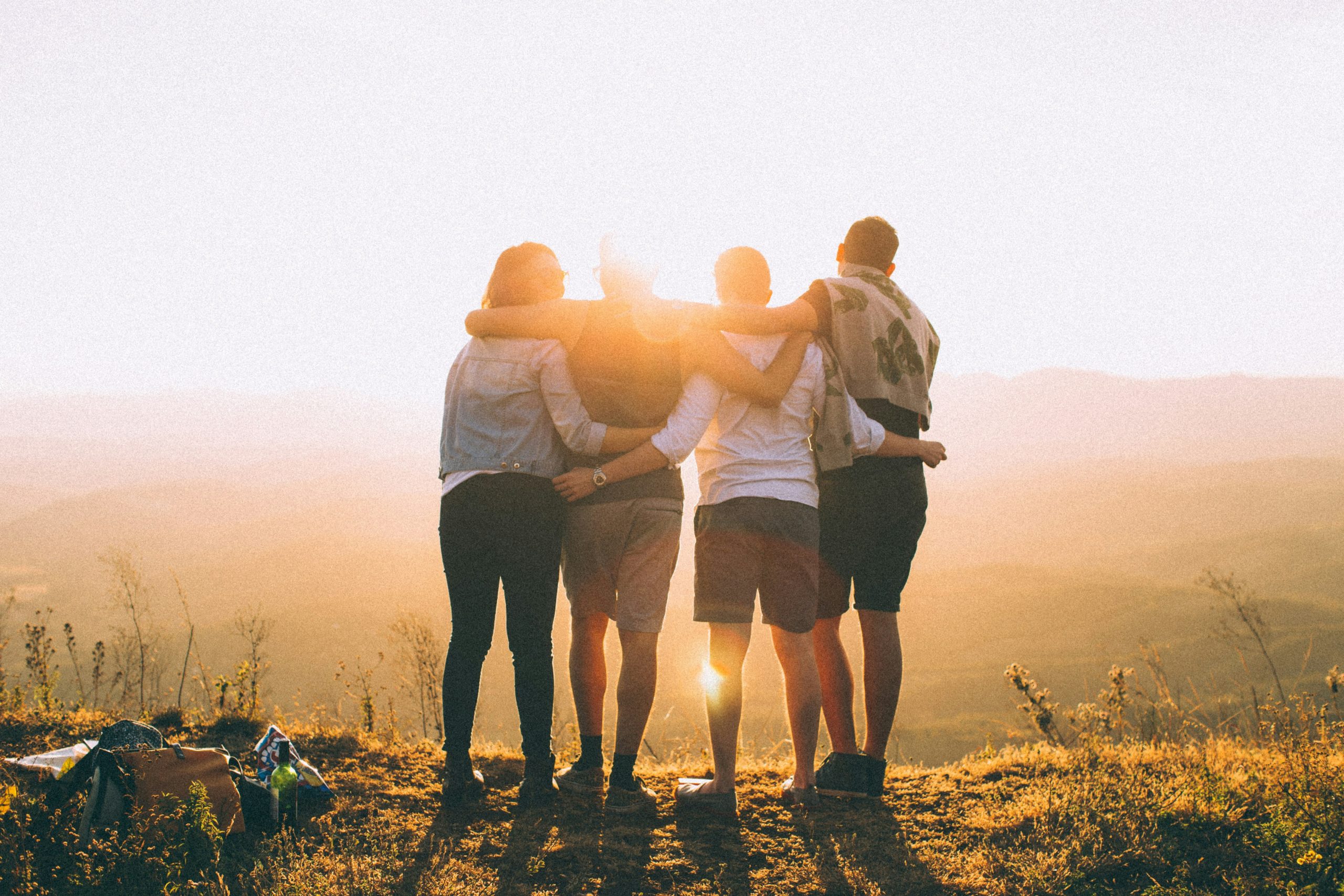four people standing with their arms around each other looking at the sunset