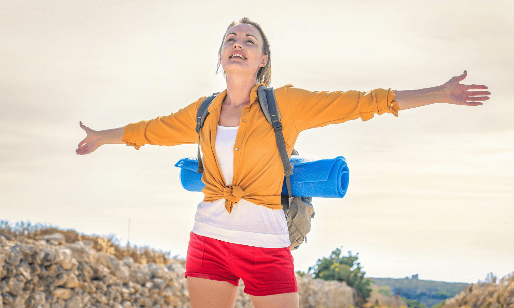 Girl with arms out to either side smiling while hiking.