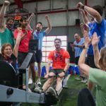 man using rowing machine at gym while fellow supporters cheer