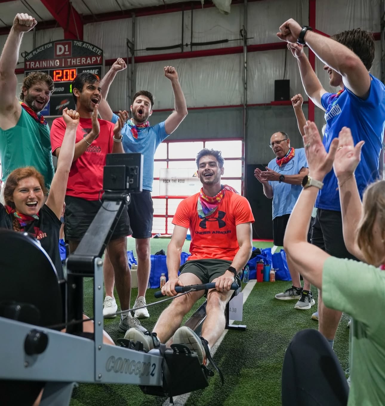 man using rowing machine at gym while fellow supporters cheer