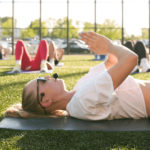 yoga instructor laying on a mat with headset during outdoor yoga class